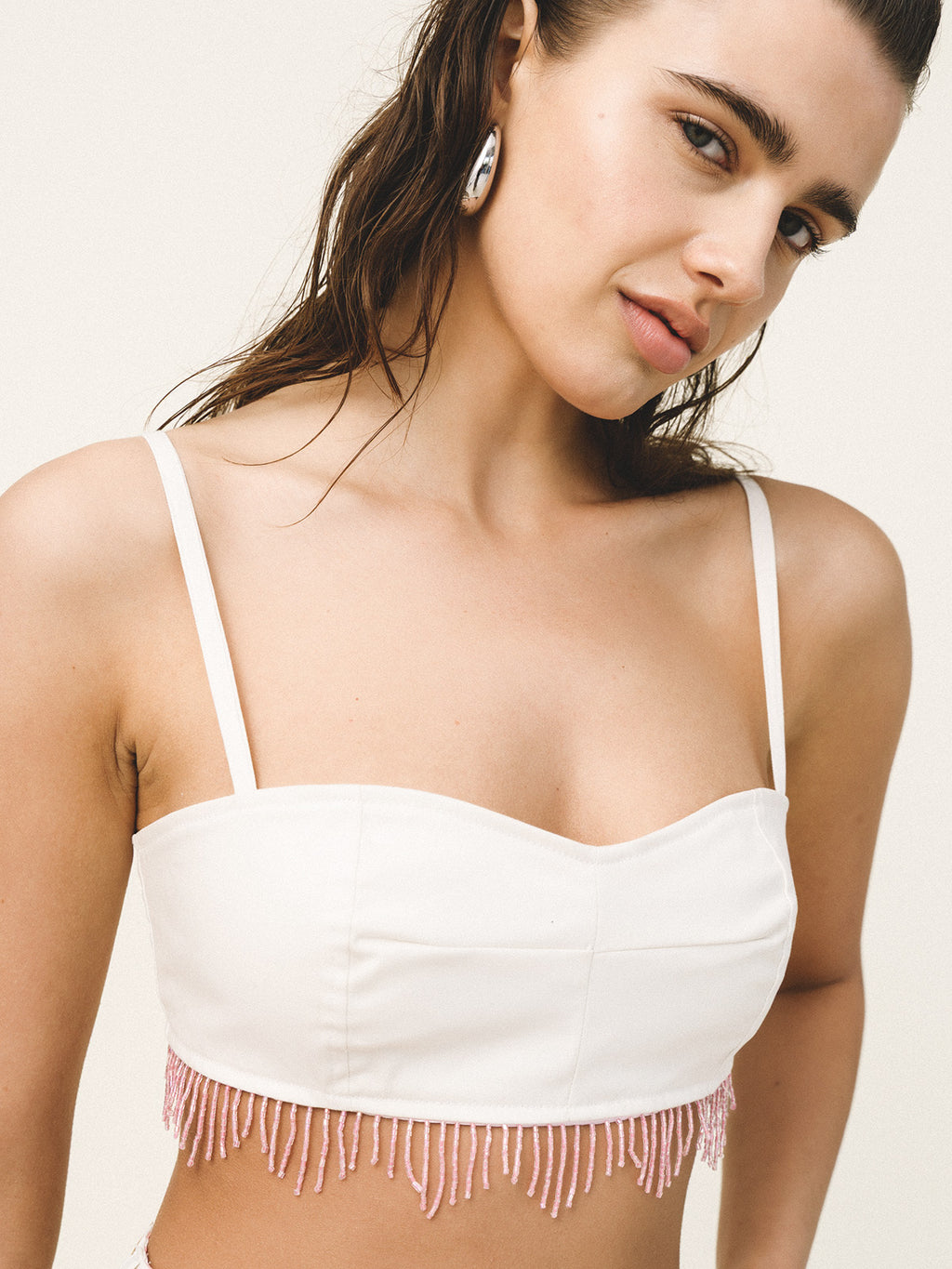Woman wearing a white top with fringe details on a plain background