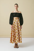 Woman wearing a black off-shoulder top and sunflower patterned skirt against a beige background