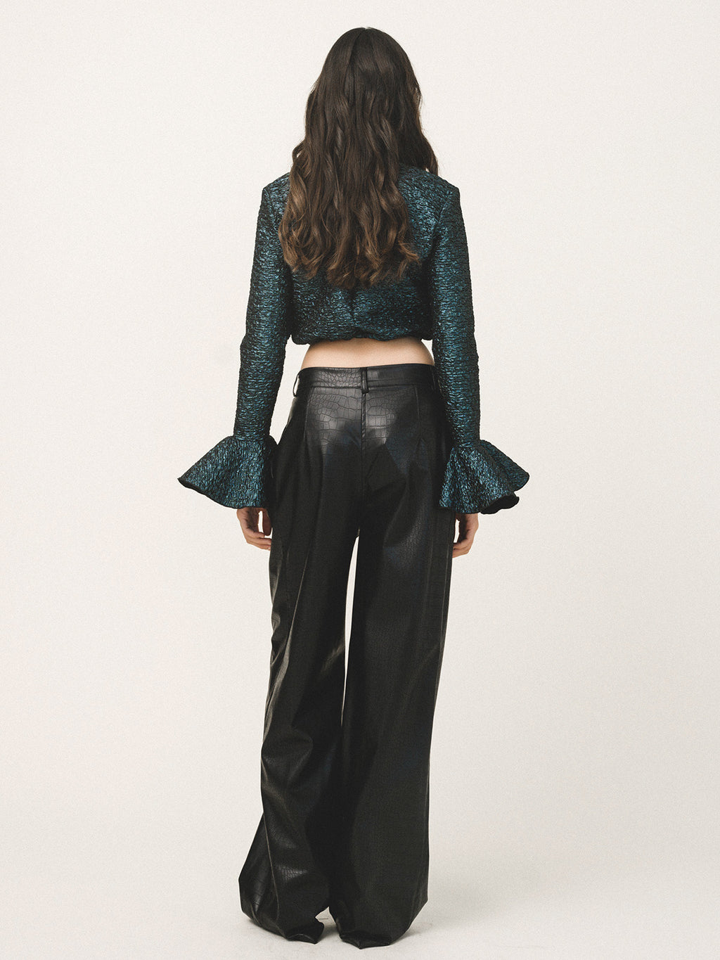 Person wearing a blue textured top and black leather pants on a white background