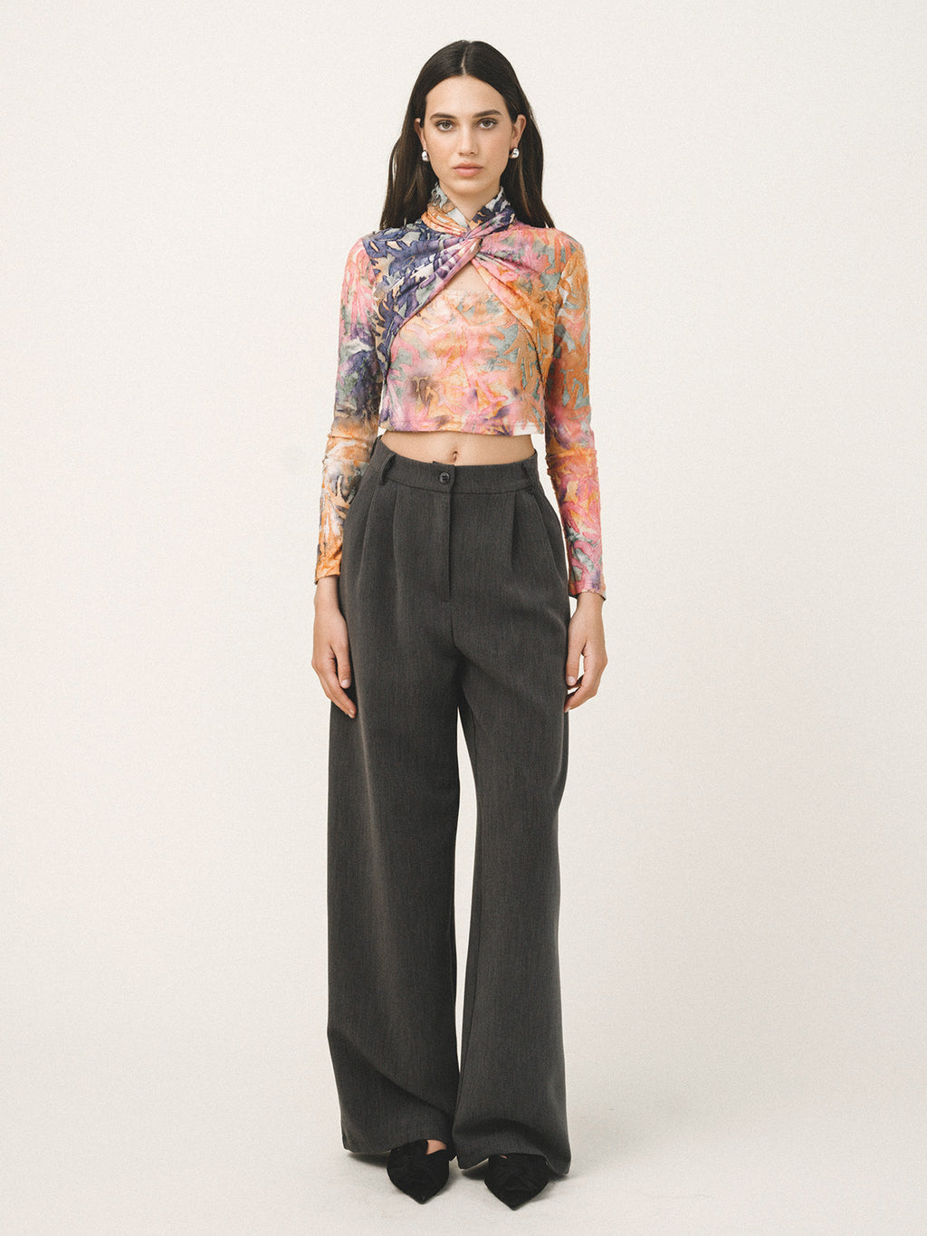 Woman wearing a colorful floral top and black high-waisted pants on a white background