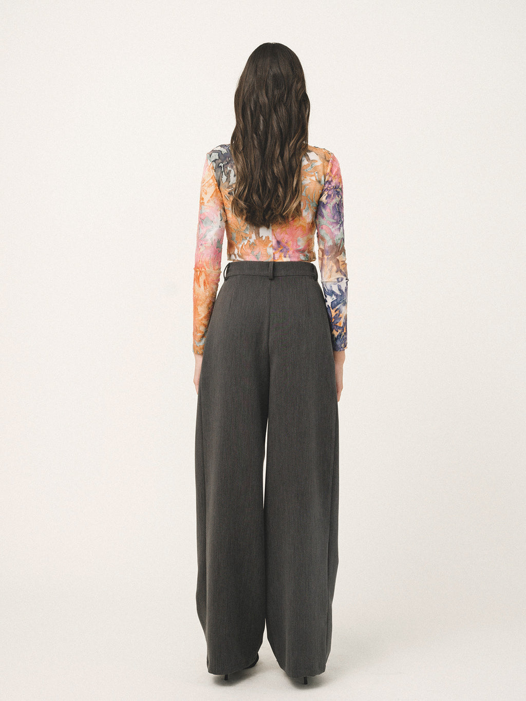Person wearing a colorful floral top and dark gray wide-leg pants on a white background