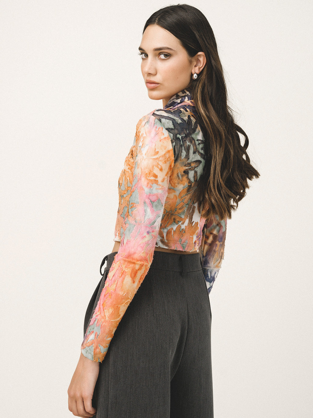 Woman wearing a colorful floral blouse with long sleeves on a plain background
