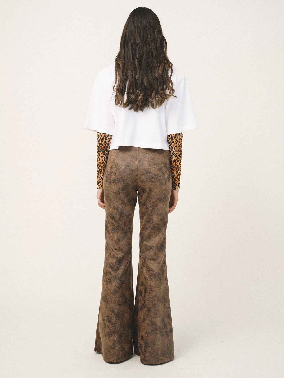 Person wearing brown flared pants and a white top with leopard print sleeves on a white background