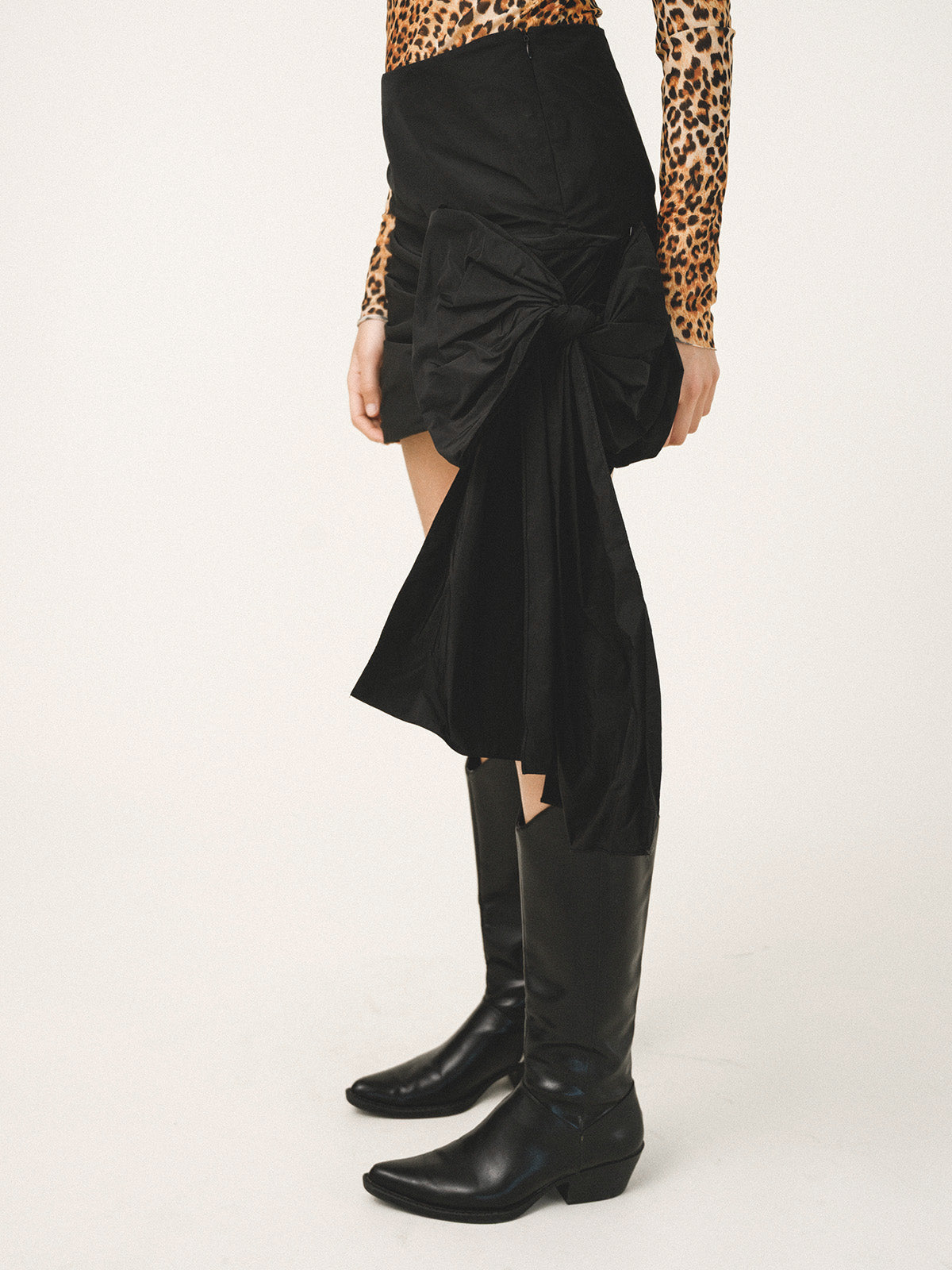 Person wearing a black skirt with cut-out sides and black knee-high boots on a white background