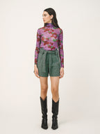 Woman wearing a floral long-sleeve top and green checkered shorts on a beige background