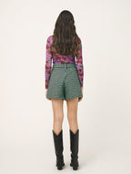 Woman wearing a floral long-sleeve top and green checkered shorts on a beige background