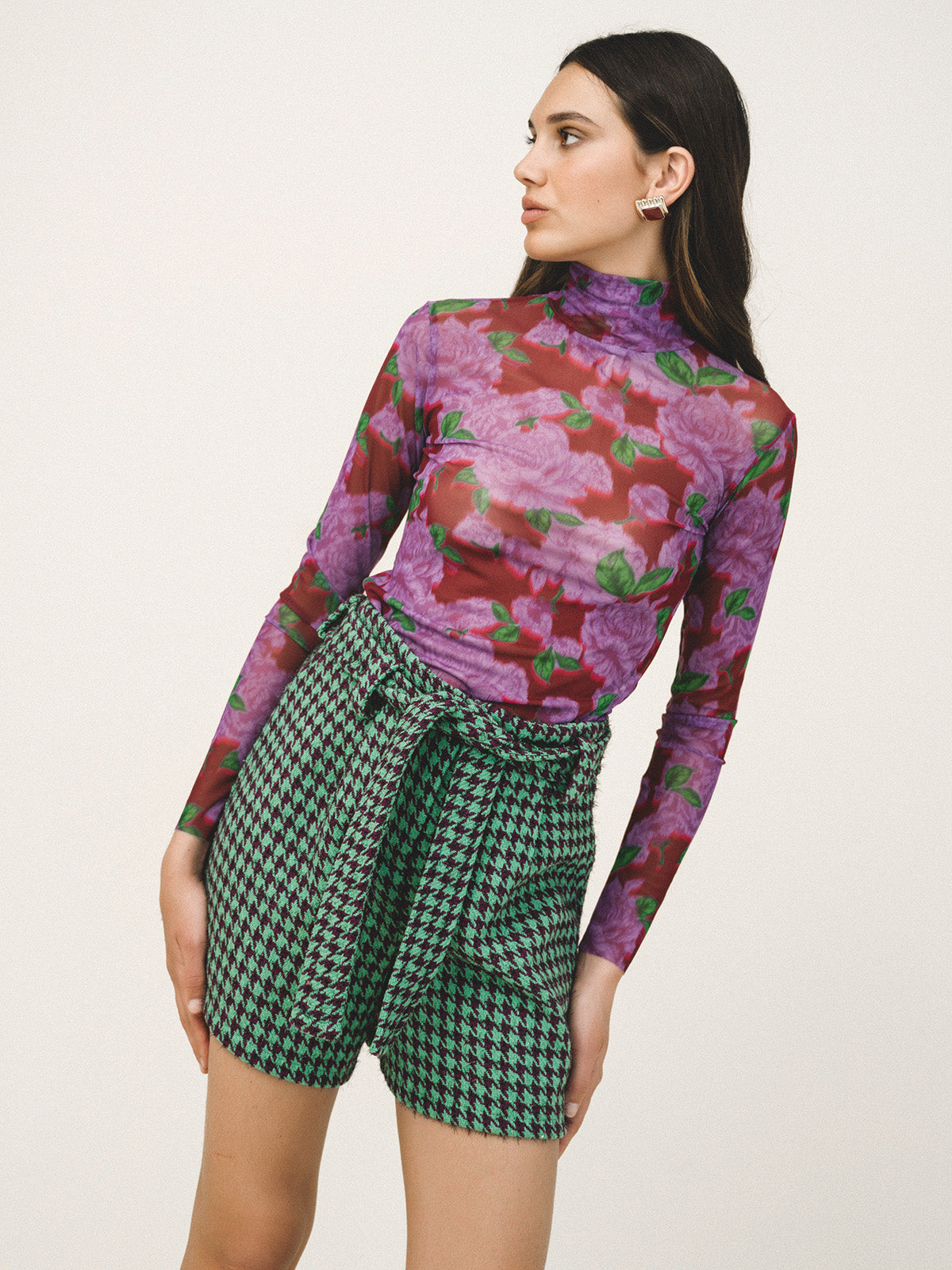 Woman wearing a floral long-sleeve top and green checkered shorts on a beige background