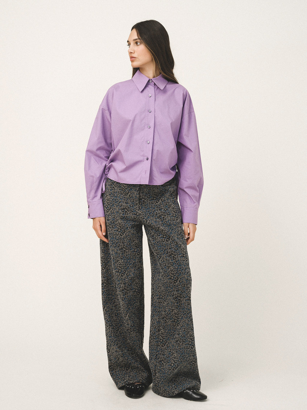 Woman wearing a purple shirt and patterned pants on a white background
