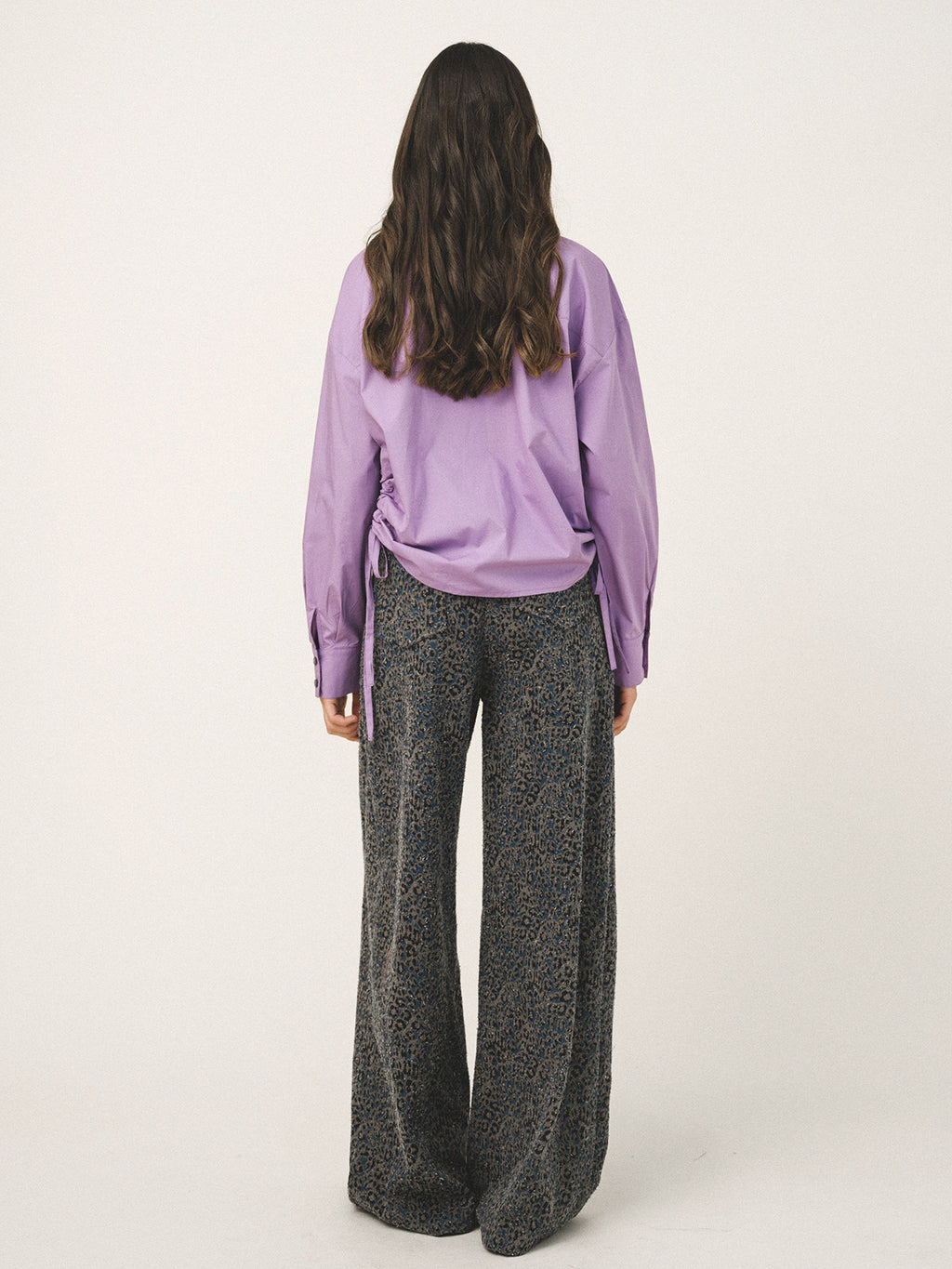 Person wearing a purple shirt and black patterned pants on a white background