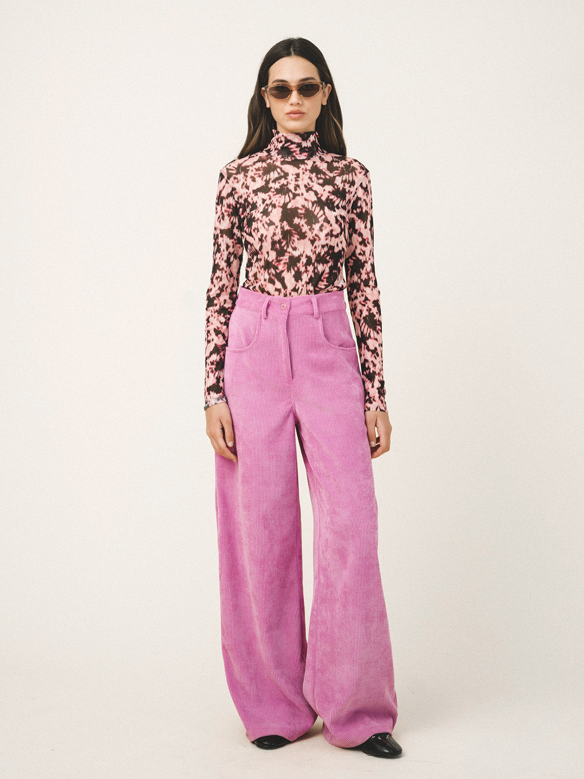 Woman wearing a floral blouse and pink pants on a white background
