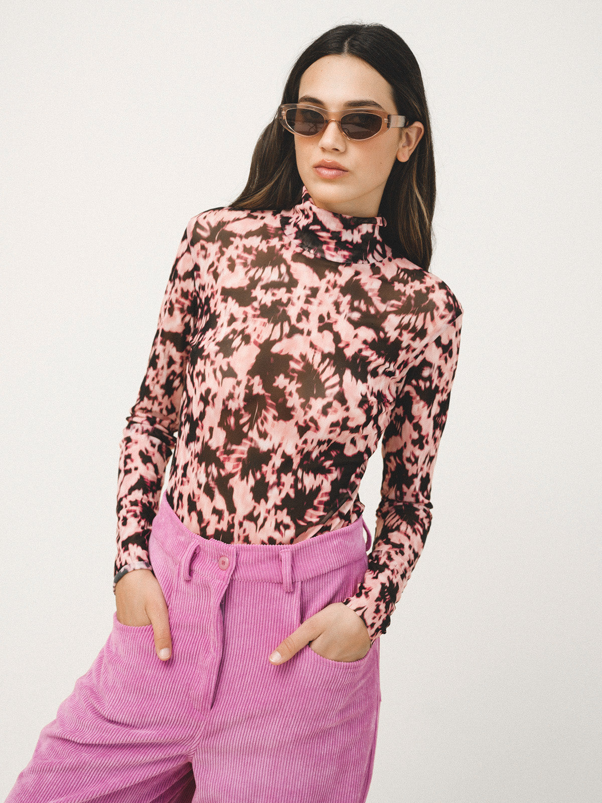 Person wearing a pink and black patterned long-sleeve top with pink pants on a white background