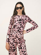 Person wearing a pink and black tie-dye outfit with sunglasses on a light background