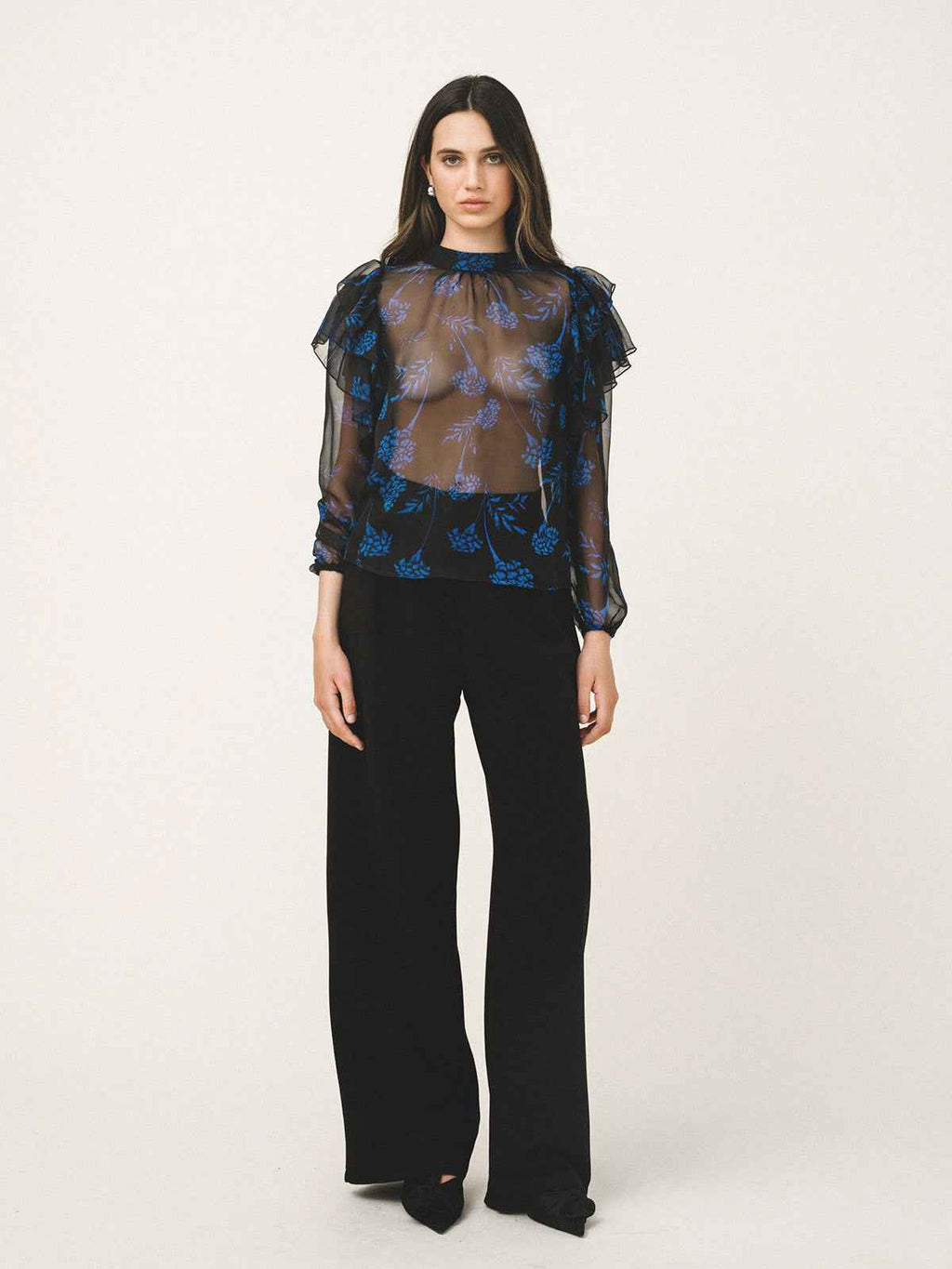 Woman wearing a sheer blue floral blouse with black pants on a white background