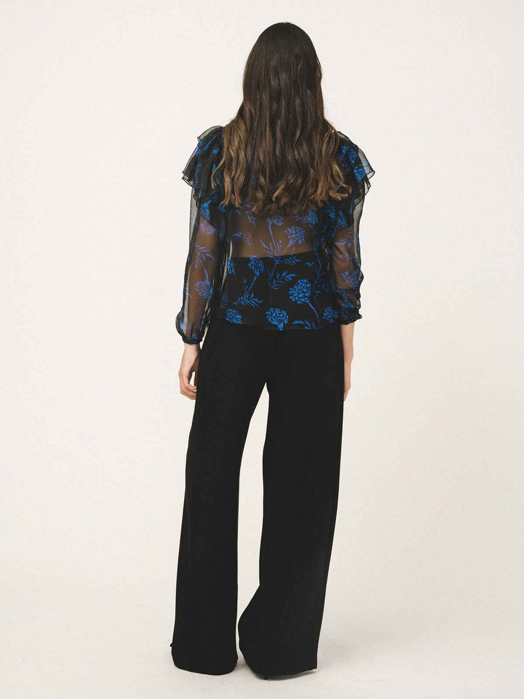 Person wearing a blue floral blouse and black pants on a white background