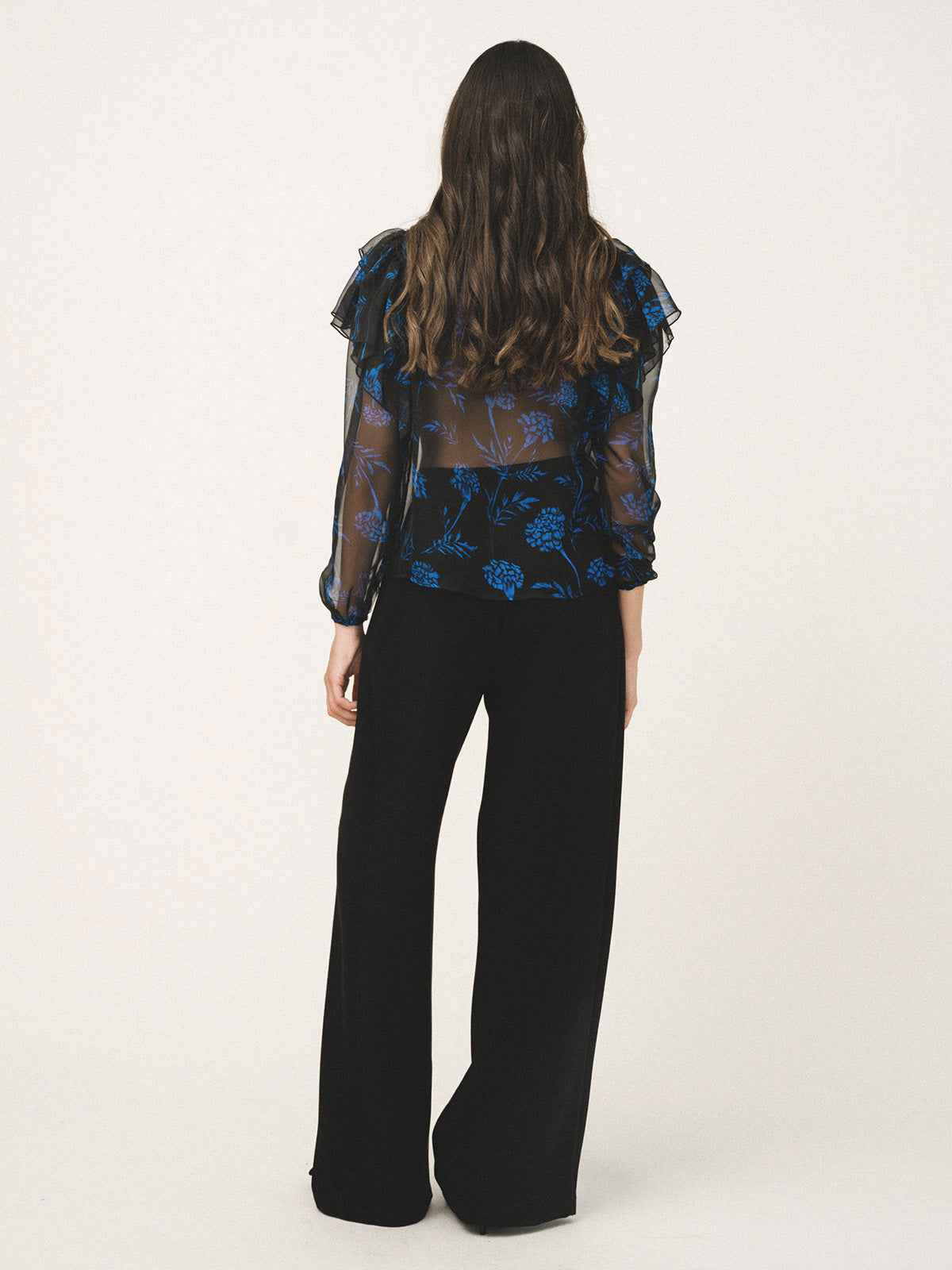 Person wearing a blue floral blouse and black pants on a white background