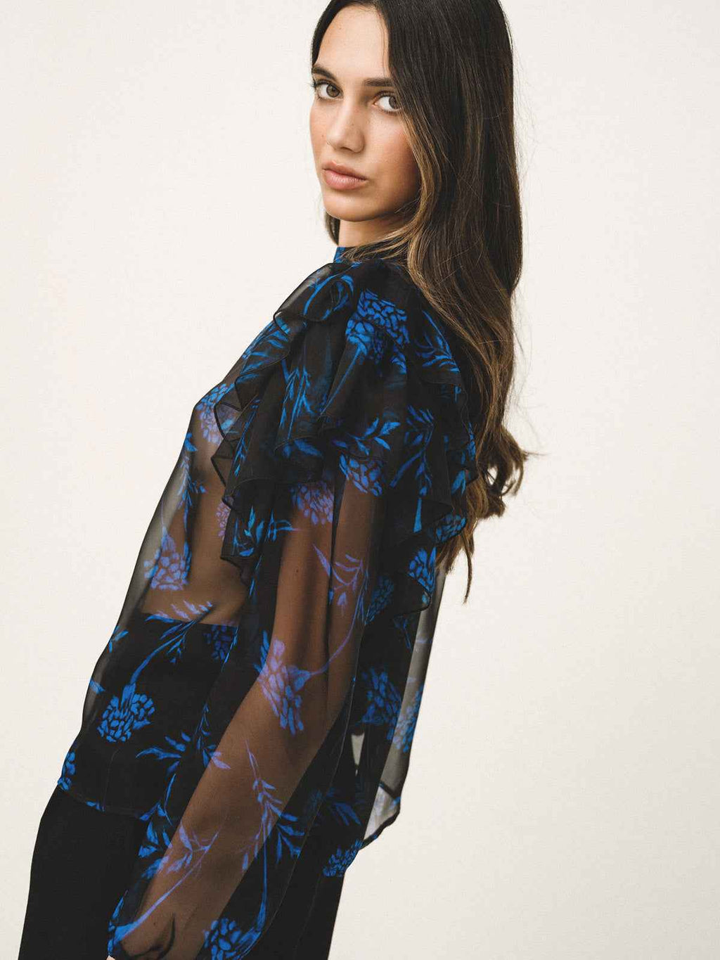 Woman wearing a black sheer top with blue floral patterns on a white background