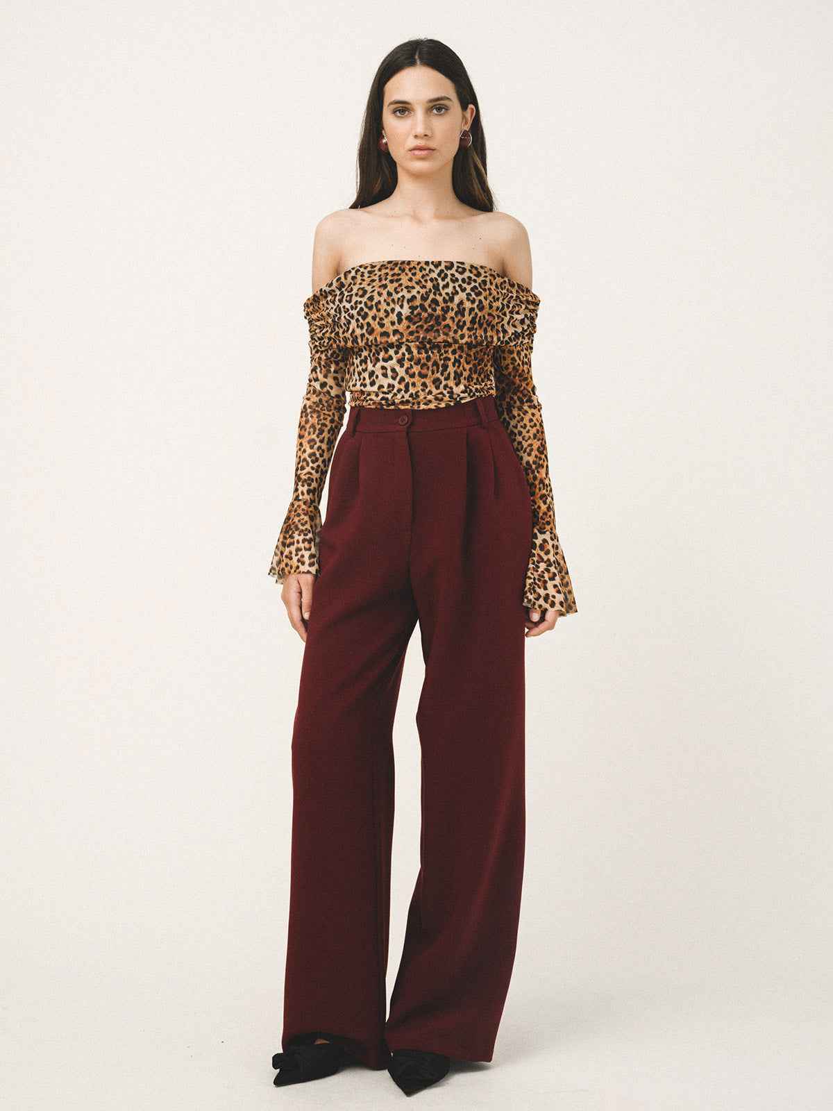 Woman wearing a leopard print top and burgundy pants on a white background