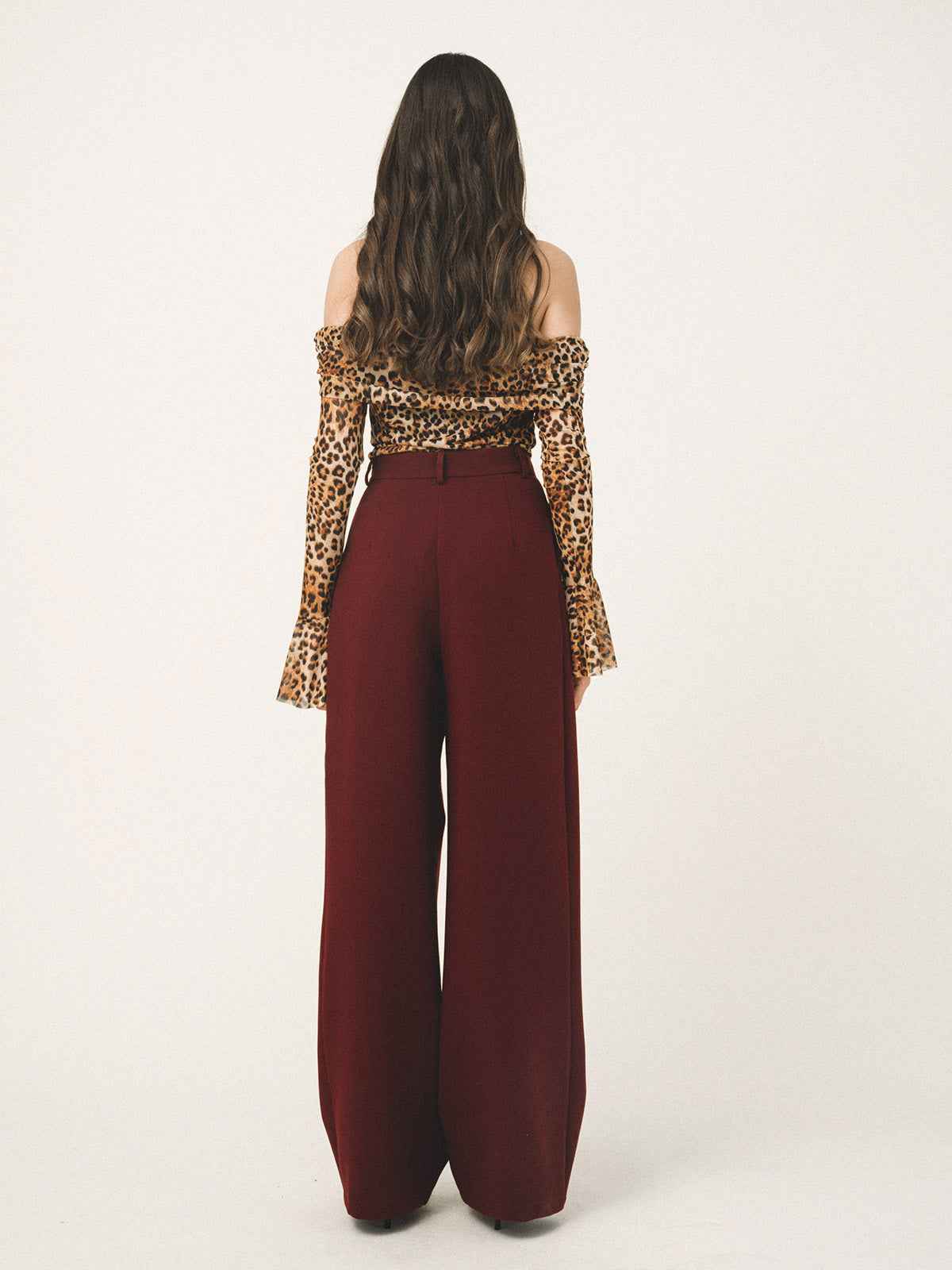 Person wearing a leopard print top and burgundy pants on a white background