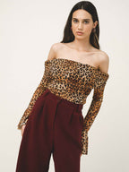 Woman wearing a leopard print off-shoulder top and burgundy pants on a white background