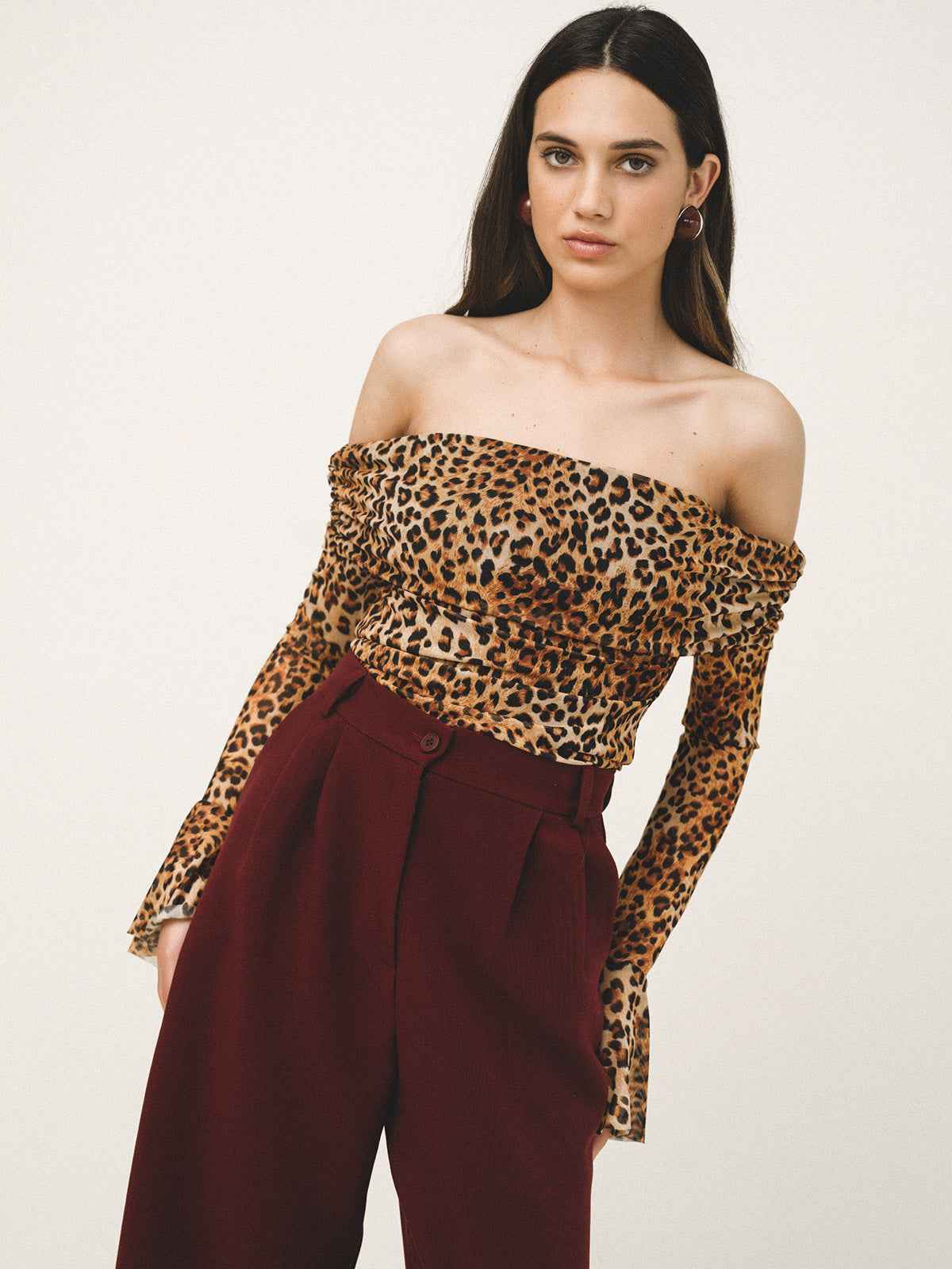 Woman wearing a leopard print off-shoulder top and burgundy pants on a white background