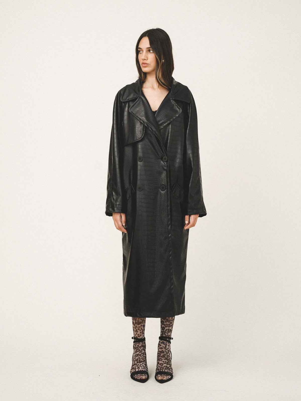 Woman wearing a long black leather coat on a white background