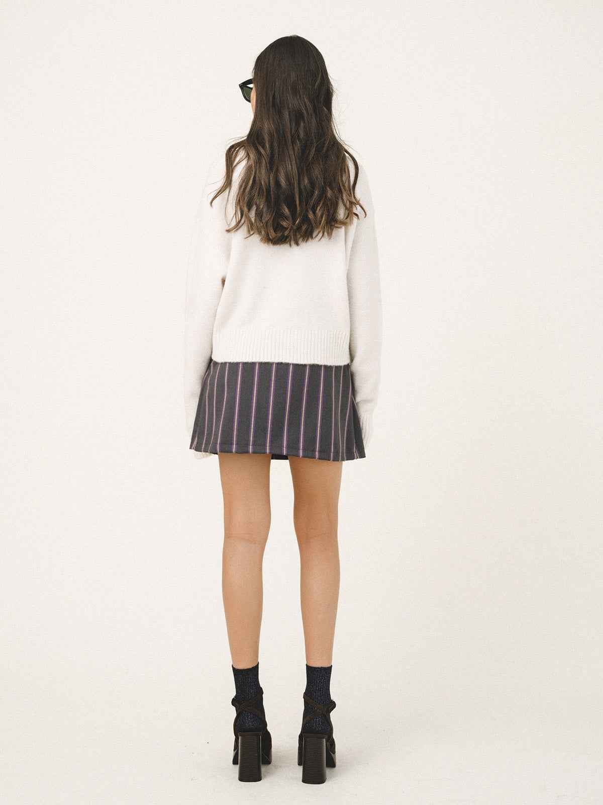 Person wearing a white sweater and striped skirt on a plain background