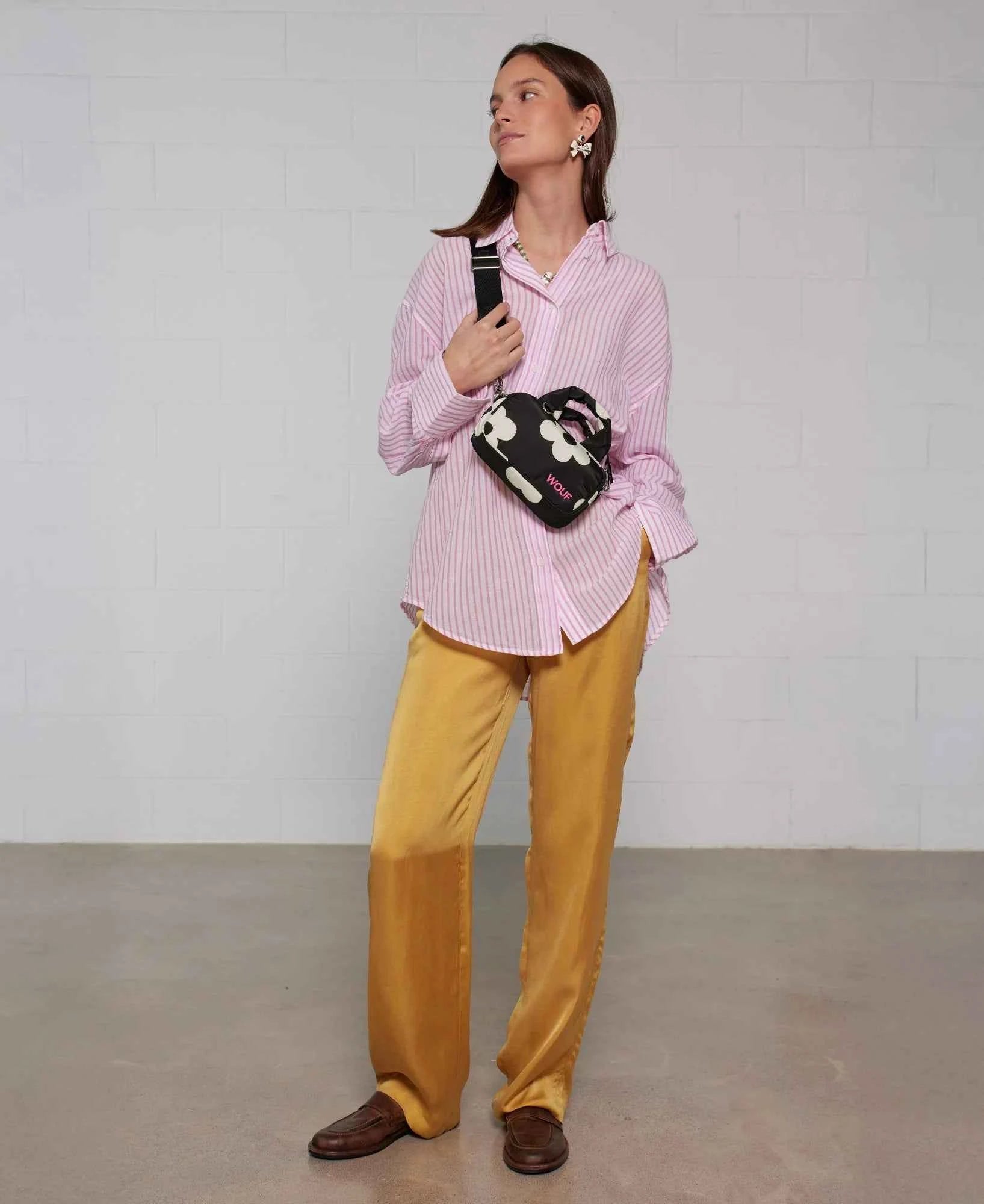 Woman wearing a pink striped shirt and yellow pants, holding a floral bag against a white background