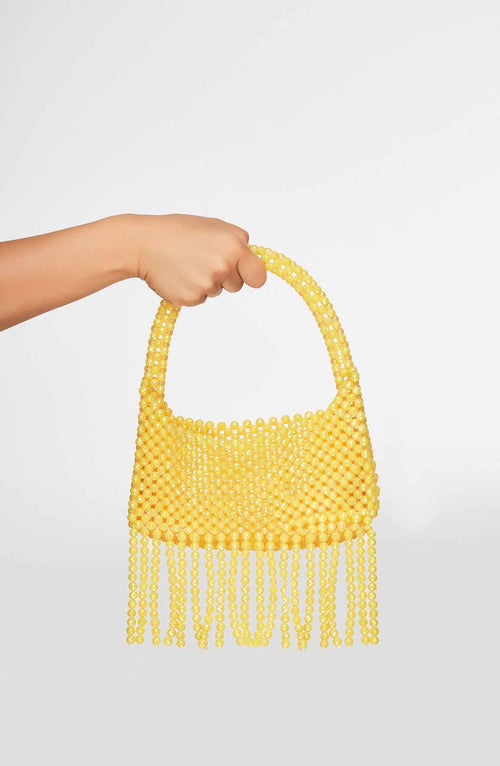 Yellow beaded handbag with fringe held by a hand on a light gray background