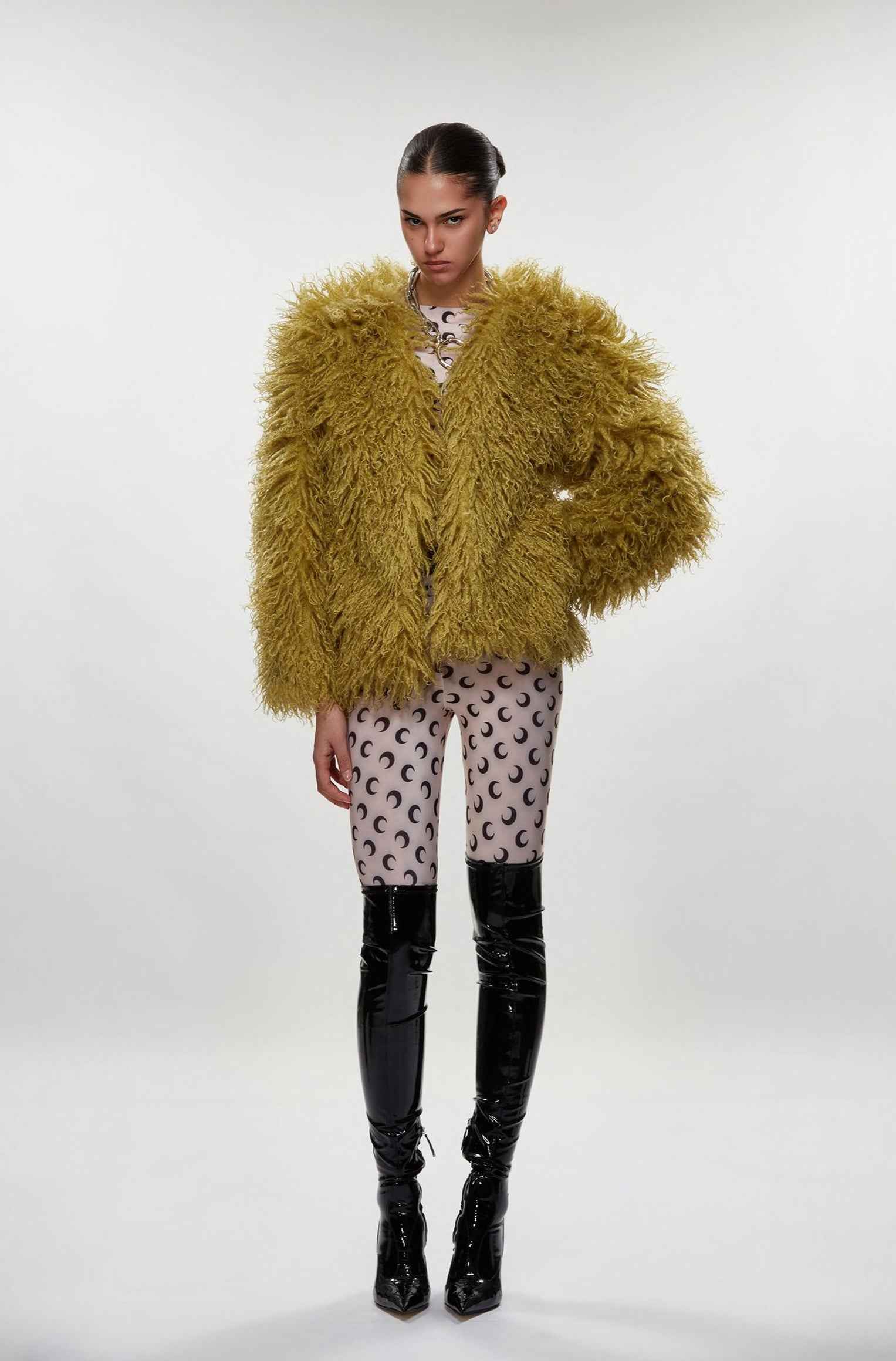 Model wearing a mustard yellow fluffy coat with black knee-high boots on a white background