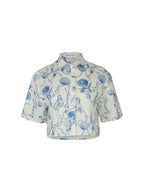 A short-sleeve button-up shirt with a blue botanical and shell pattern on a white background, shown against a plain white studio backdrop.