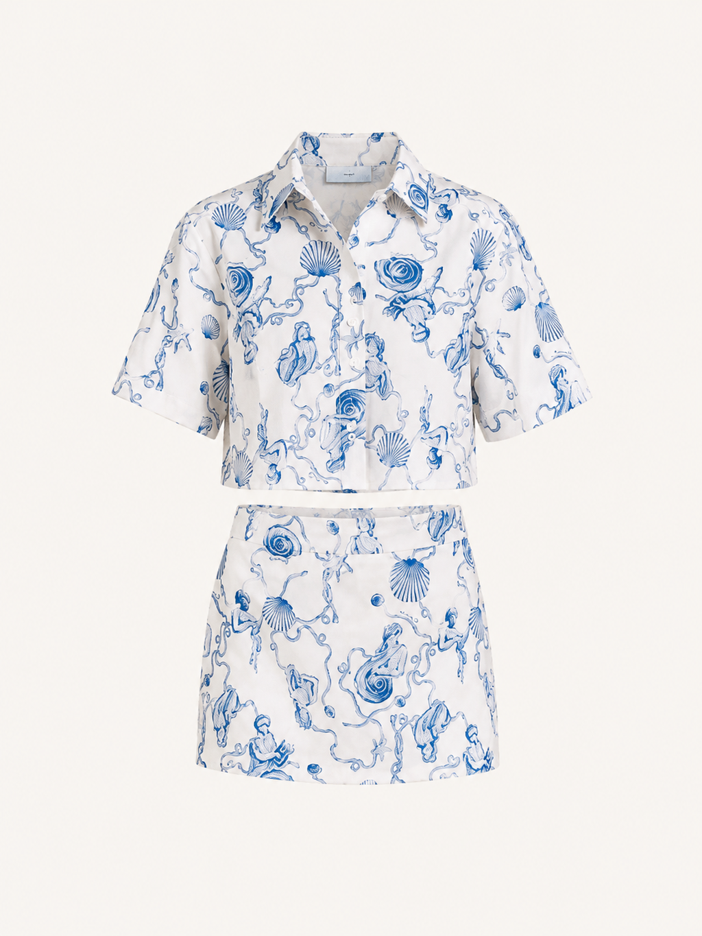 A matching two-piece set featuring a short-sleeve button-up shirt and a high-waisted mini skirt, both in white fabric with a blue toile-style print of sea creatures, shells, and waves. The set is displayed on a clean, solid off-white background.