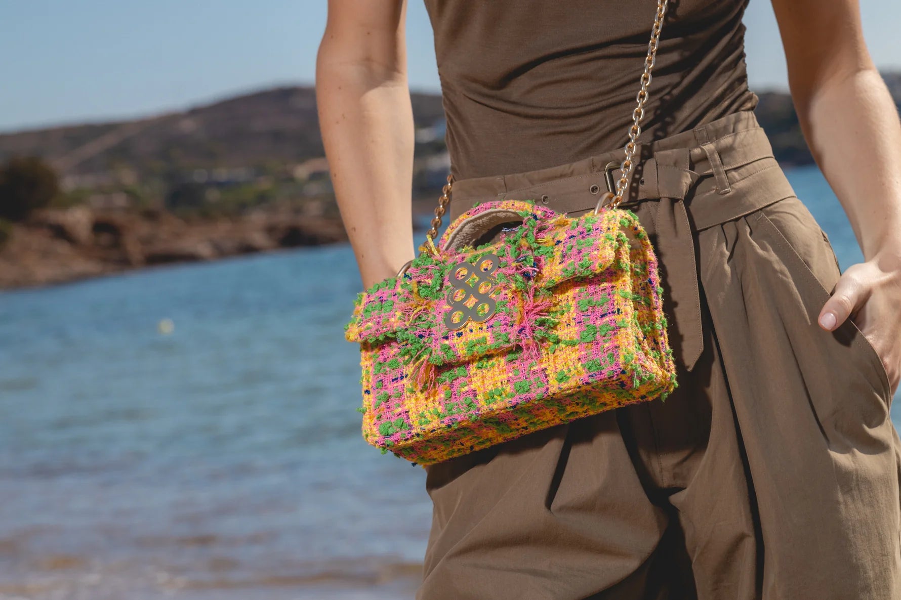Person holding a colorful handbag by a body of water