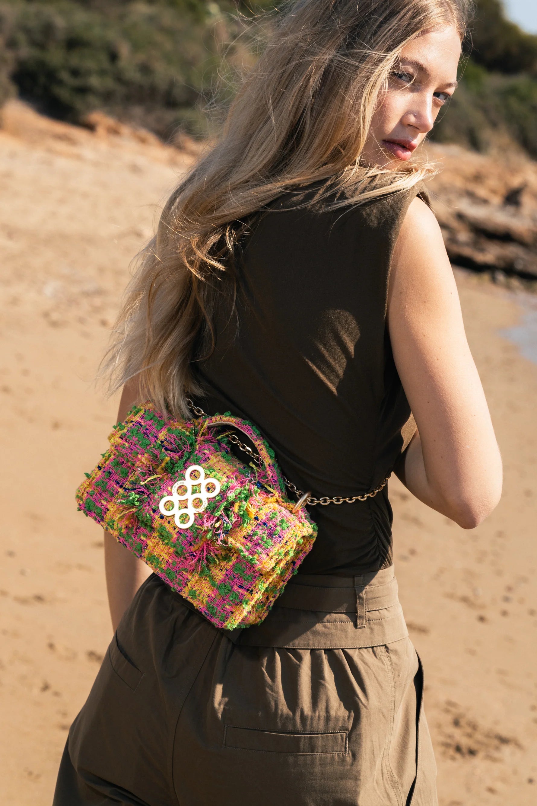Woman on a beach wearing a colorful handbag with a logo.