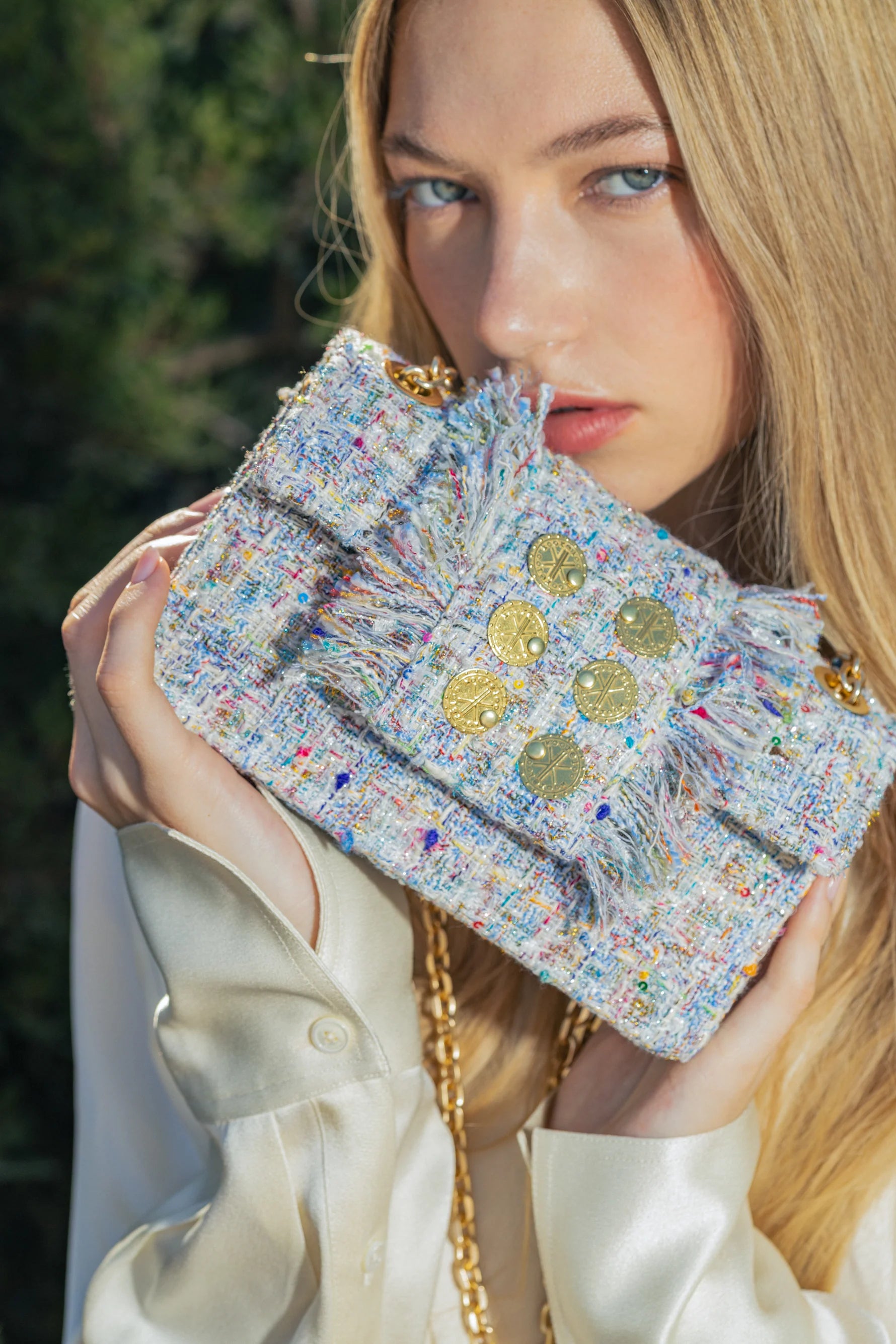 Woman holding a colorful textured clutch with a blurred natural background