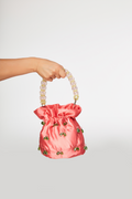 Pink drawstring bag with pearl handle held by a hand on a light gray background