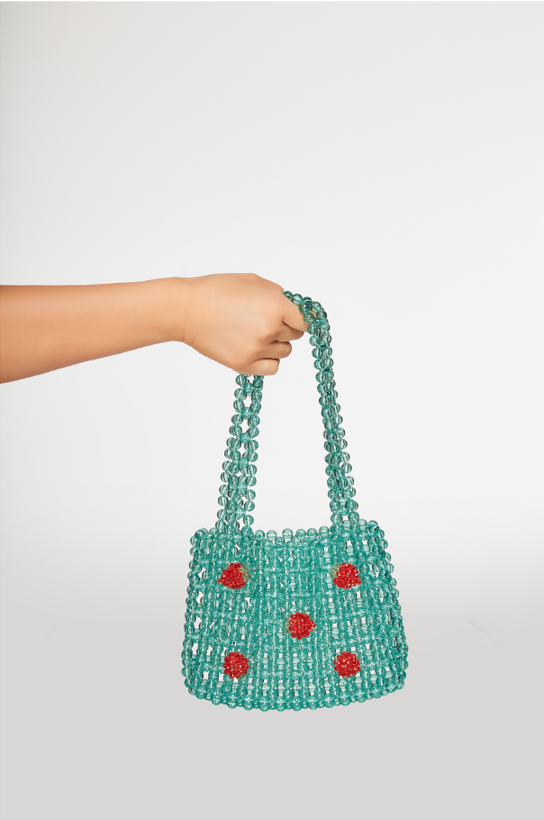 Turquoise beaded handbag with red accents held by a hand on a white background