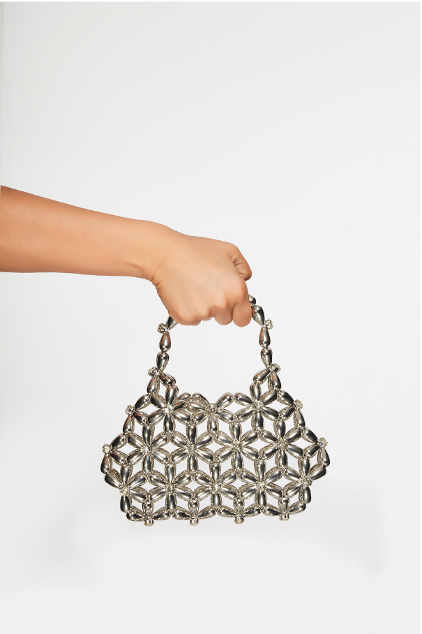 Hand holding a silver woven handbag against a white background