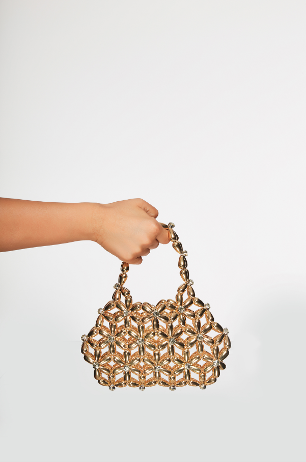 Hand holding a gold handbag against a white background