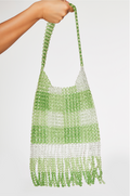 Green and white beaded bag held by a hand on a light gray background
