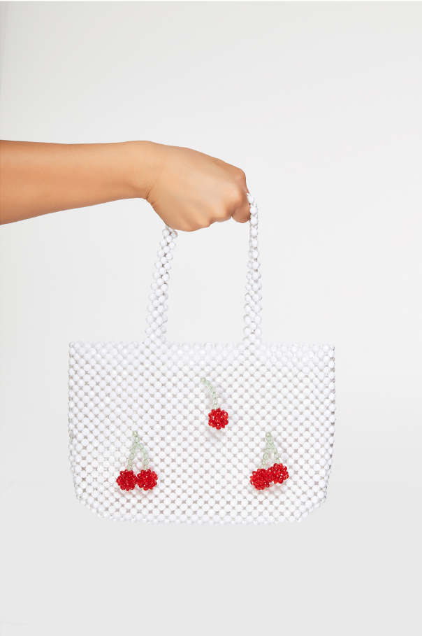 Hand holding a white mesh bag with red cherry designs on a white background