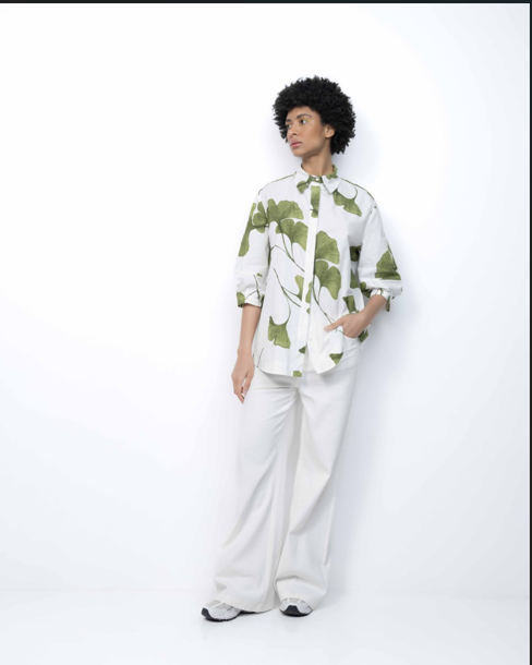 Person wearing a white shirt with green patterns and white pants on a white background