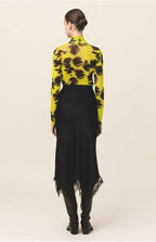Person wearing a yellow and black floral top with a black skirt on a beige background