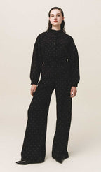A person standing wearing black carduroy pants with Stone embellishments and a wide-leg, mid-rise fit.