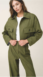 A woman wearing a green button-up crop jacket with large flap pockets and a white top.