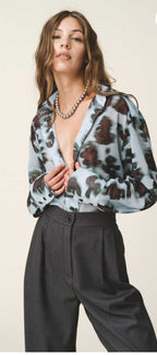 A model wearing an oversized sheer shirt with a geometric animal pattern, featuring a loose fit and buttoned cuffs, paired with a matching long skirt.