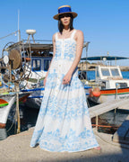 Woman in a blue and white floral dress standing on a dock with boats in the background