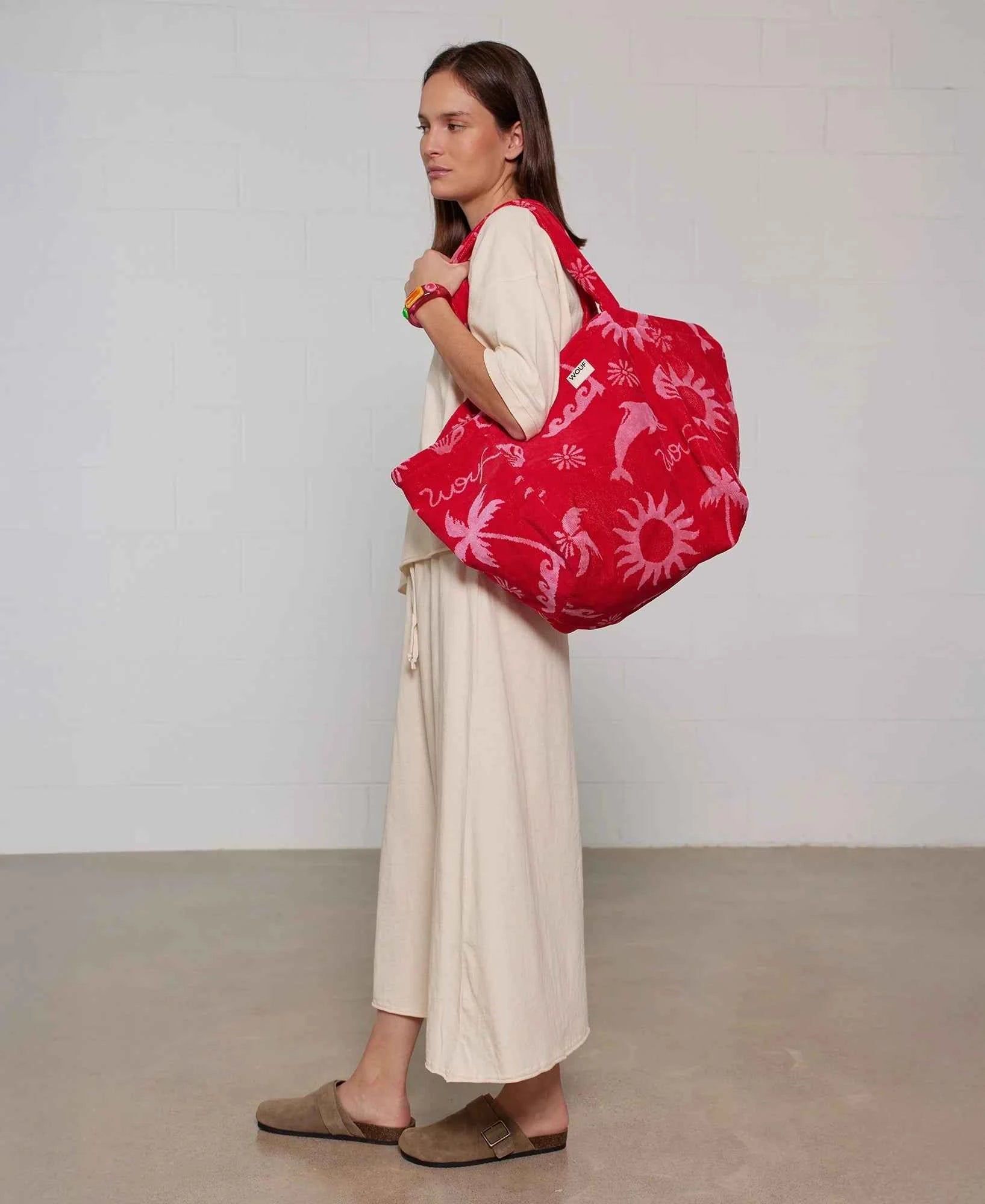 Woman holding a red patterned bag against a plain background