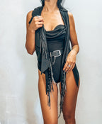 Woman wearing a black fringe vest over a black top with a plain background
