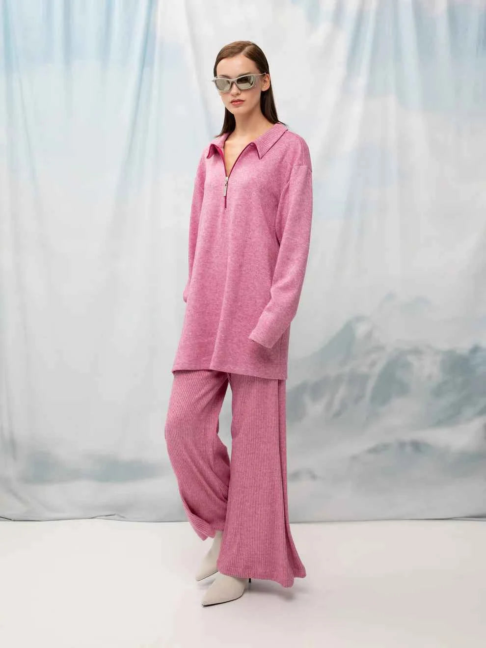 Woman wearing a pink outfit with sunglasses against a white background