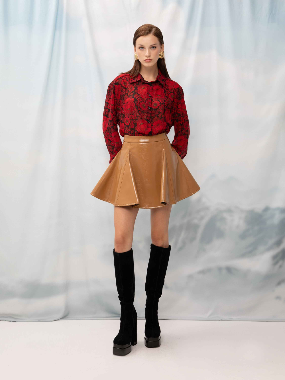 Woman wearing a red floral blouse, tan skirt, and black knee-high boots against a white background